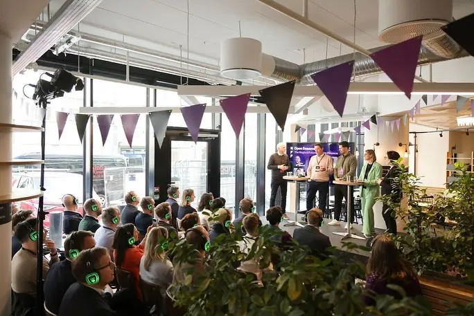 Panelsamtale i lyst lokale med vimpler og publikum med hodetelefoner