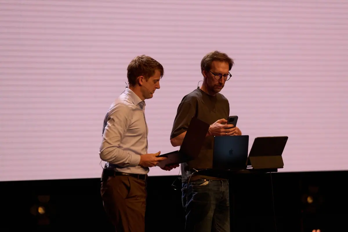 To programledere forbereder seg med nettbrett og laptop på scenen