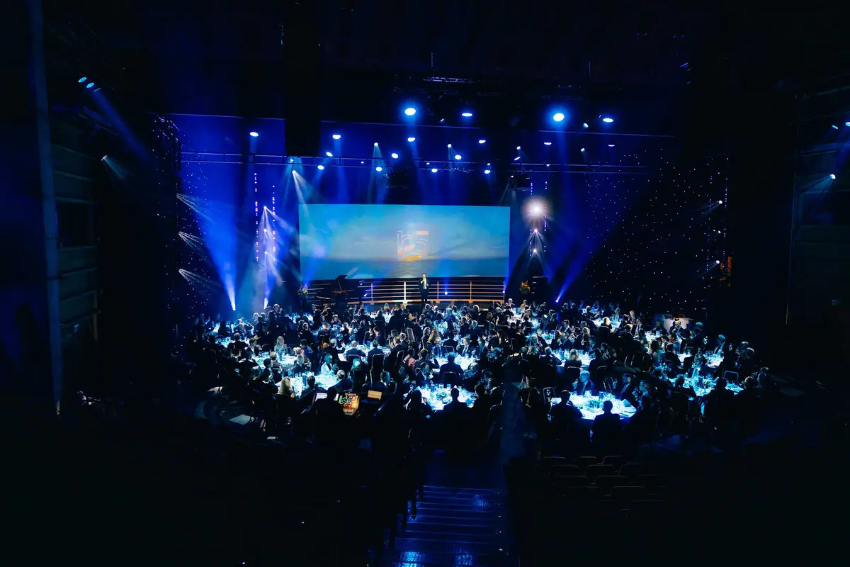 Festmiddag med runde bord i blått lys foran scenen på Bergens Rederiforenings jubileum