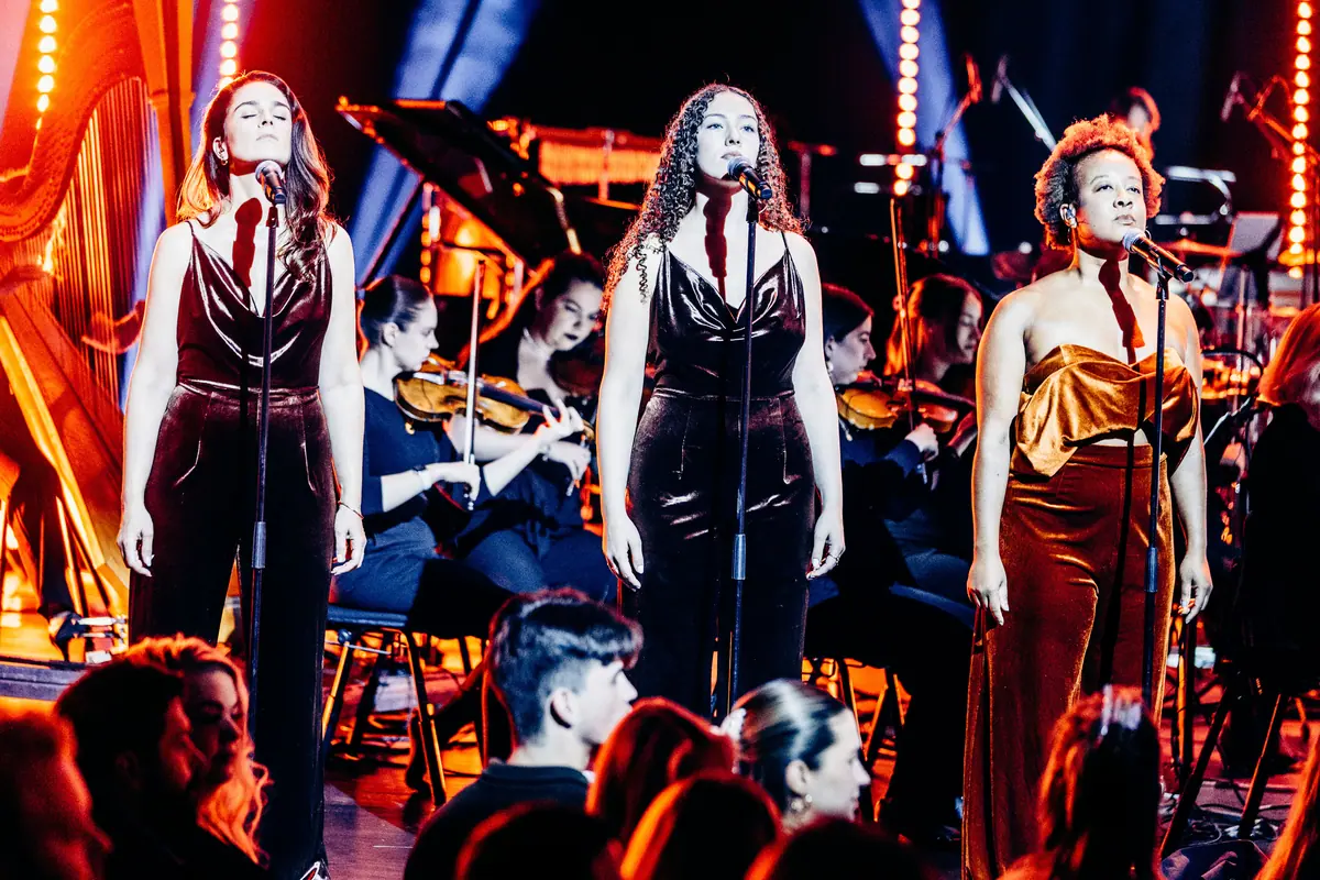 Tre vokalister i fløyelskjoler synger foran orkesteret under Red Bull Symphonic