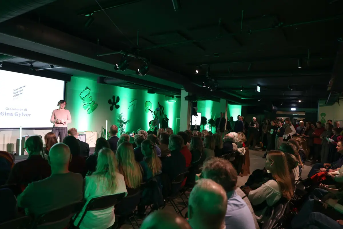 Fullsatt sal med publikum foran en scene i grønt lys under Klimafestivalen