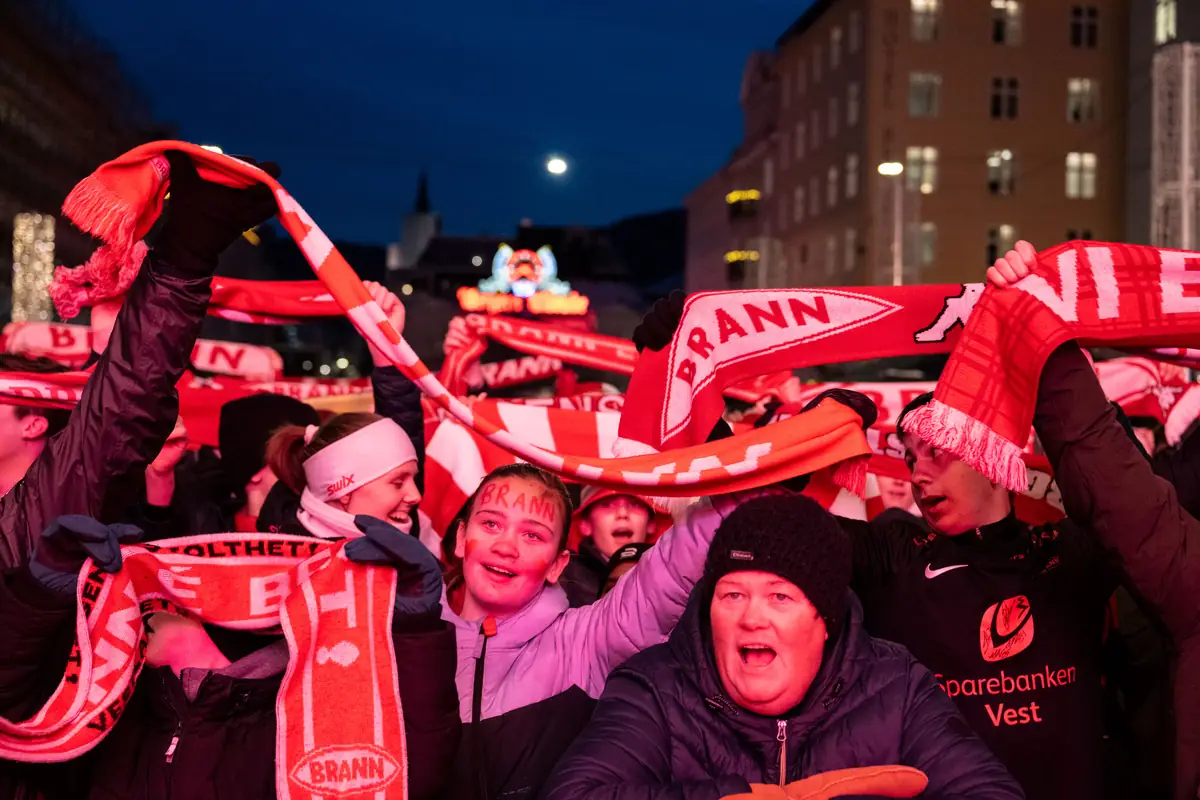 Brann-supportere med rødt og hvitt skjerf heier på Torgallmenningen i kveldsmørket