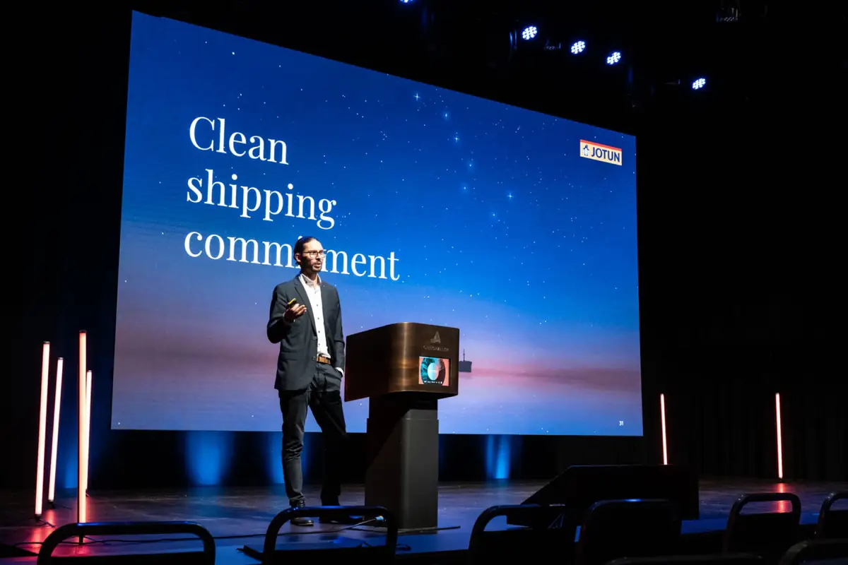Foredragsholder ved talerstol foran stor skjerm med teksten «Clean shipping commitment»