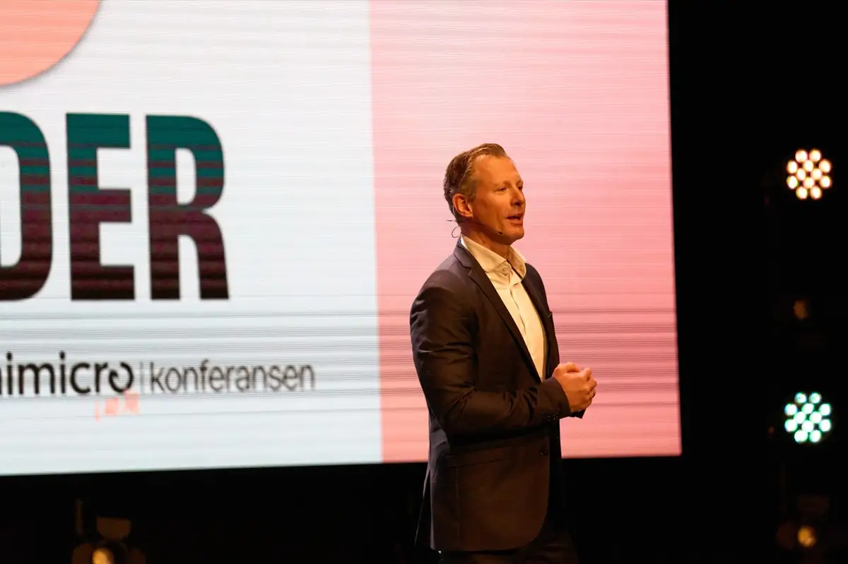 Foredragsholder på scenen foran storskjerm under Unimicro Byråkonferansen