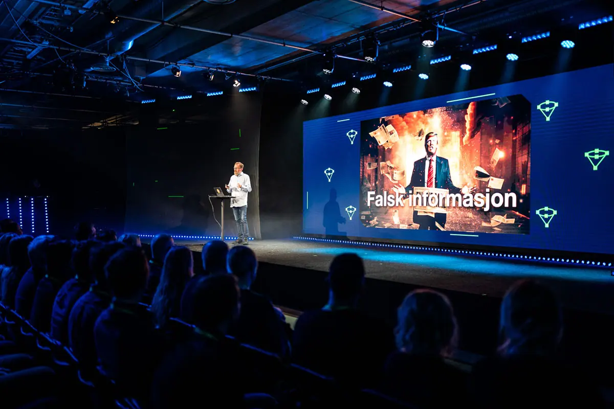 Foredragsholder på Volum-scenen foran storskjerm med «Falsk informasjon»