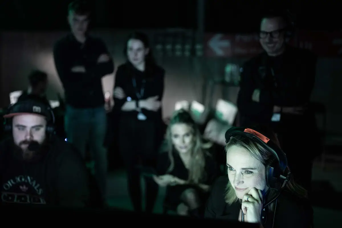 Produksjonsteam med headset følger med på skjermer i mørket bak scenen